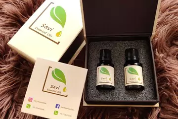 two bottles of savi essential oil packaged in a box, placed on a rug.